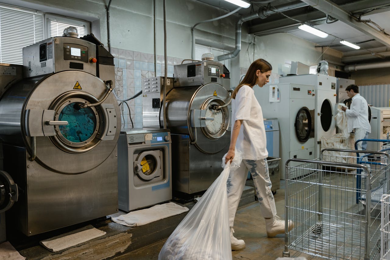 Busy industrial laundry with workers handling large washing machines.
